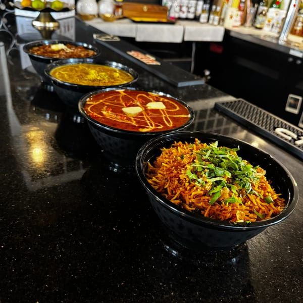 Four bowls of Indian food, including rice and curries, lined up on a dark bar counter.
