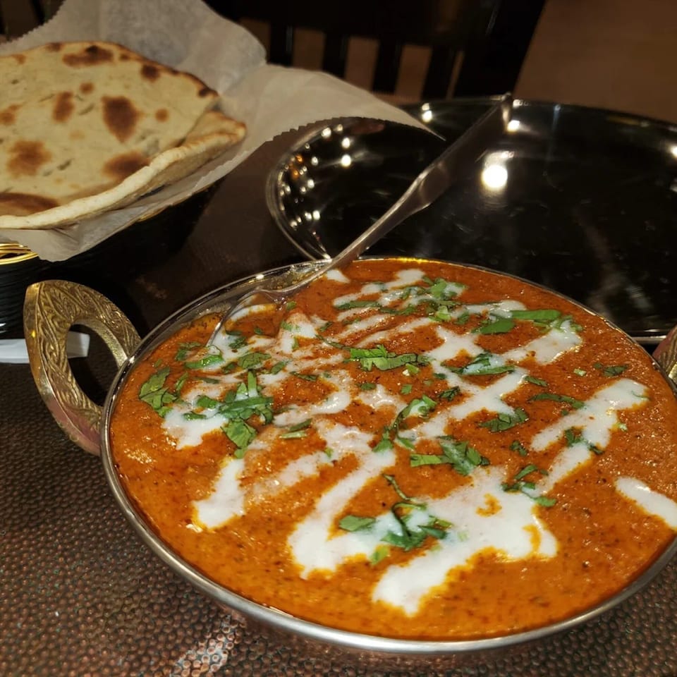 A bowl of Indian butter chicken with cream and cilantro, served with naan bread.