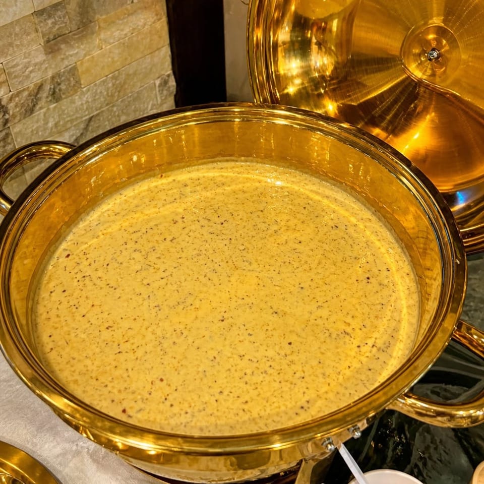 Creamy yellow soup with dark specks in a large, ornate golden serving dish.