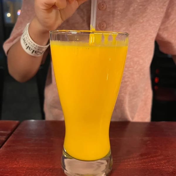 A person stirring a vibrant yellow mango lassi in a tall glass at Spice Kitchen.