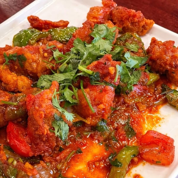 Spicy red chicken dish with green peppers, tomatoes, and cilantro on a white plate.
