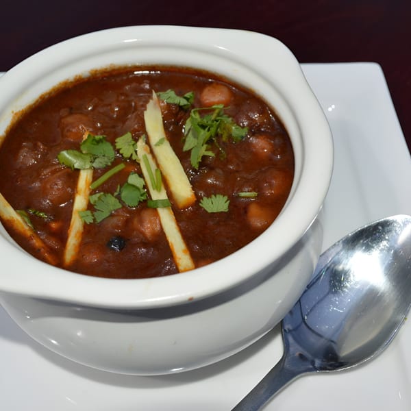 A white bowl of Indian chana masala, garnished with cilantro and ginger, on a white plate.
