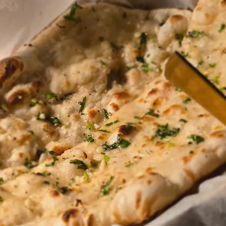 Close-up of golden-brown naan bread, sprinkled with fresh green herbs and spices, from Spice Kitchen.