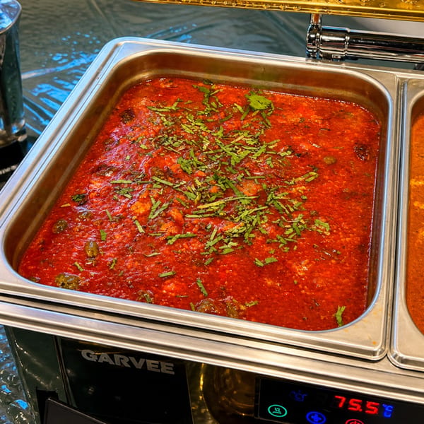 Vibrant red curry topped with fresh green herbs in a buffet chafing dish.