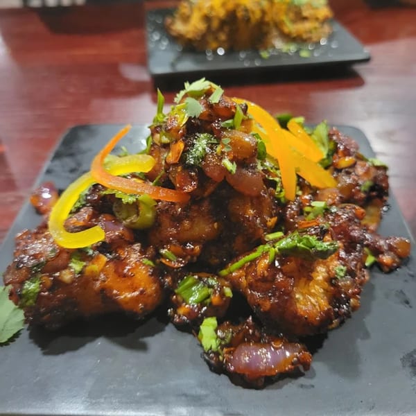 Indian chili chicken on a black plate, garnished with bell peppers, onions, and cilantro.