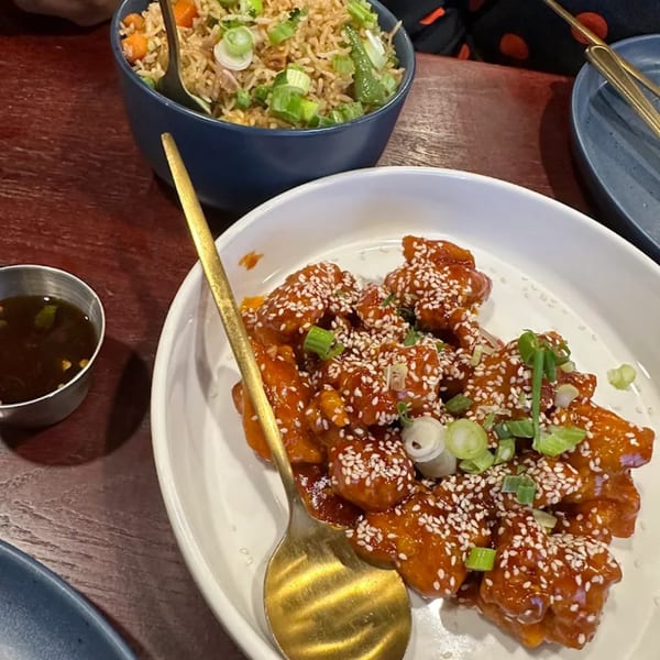 Sweet and sour chicken with sesame seeds and scallions, alongside a bowl of fried rice.