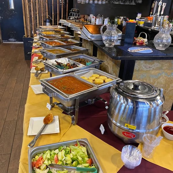 A long buffet table at Spice Kitchen filled with various Indian dishes in chafing dishes and a salad.
