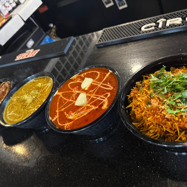 Three bowls of Indian food, including rice and two curries, on a dark counter.