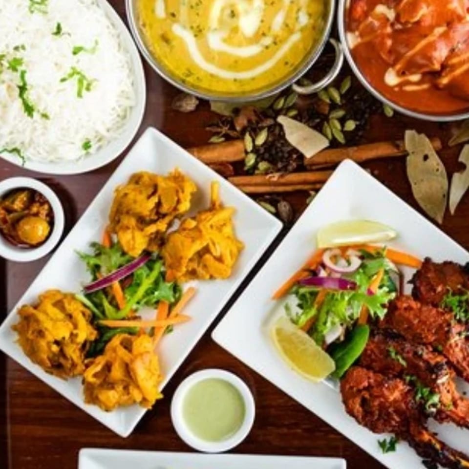 A vibrant Indian feast from Spice Kitchen, featuring curries, rice, pakoras, and grilled lamb chops.
