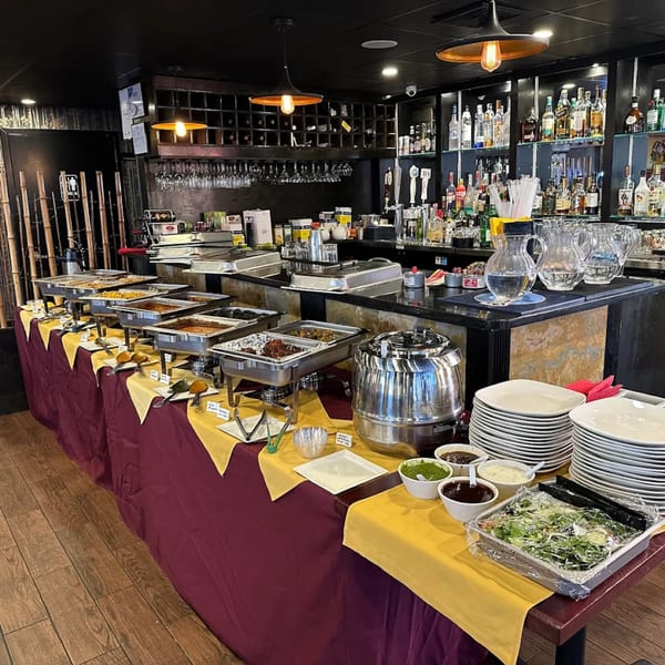 Spice Kitchen's Indian buffet features chafing dishes of food, a bar with liquor bottles, and stacked plates.