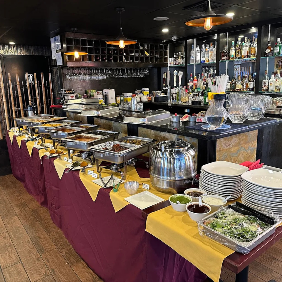 Spice Kitchen's Indian buffet features chafing dishes of food, a bar with liquor bottles, and stacked plates.