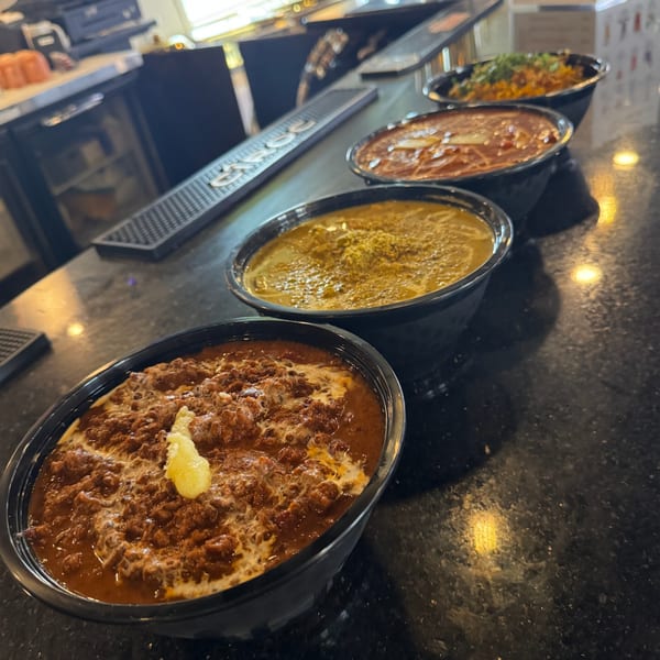 Four bowls of Indian curries and rice dishes lined up on a dark bar counter.