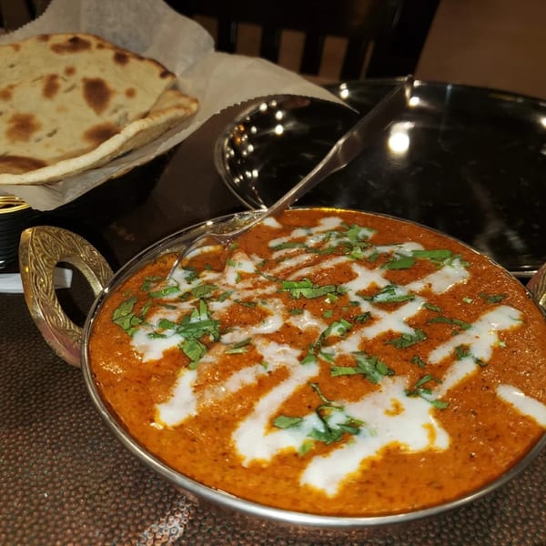 A bowl of Indian butter chicken with cream and cilantro, served with naan bread.