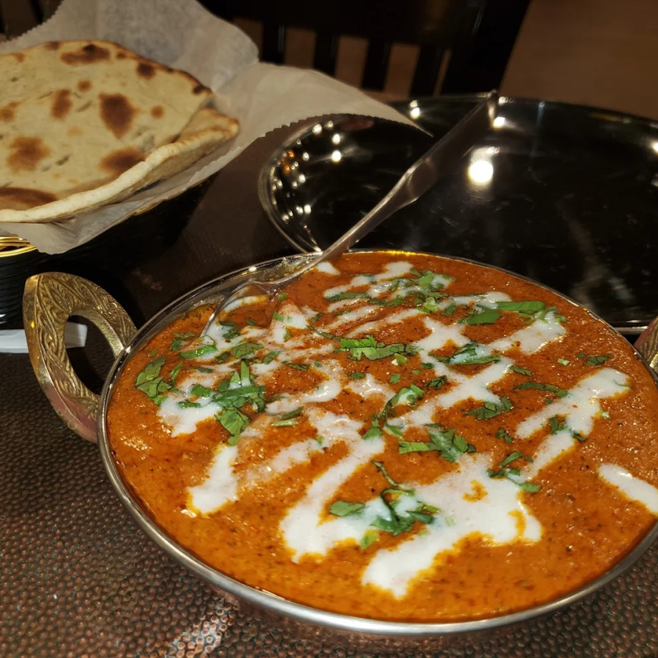 A bowl of Indian butter chicken with cream and cilantro, served with naan bread.