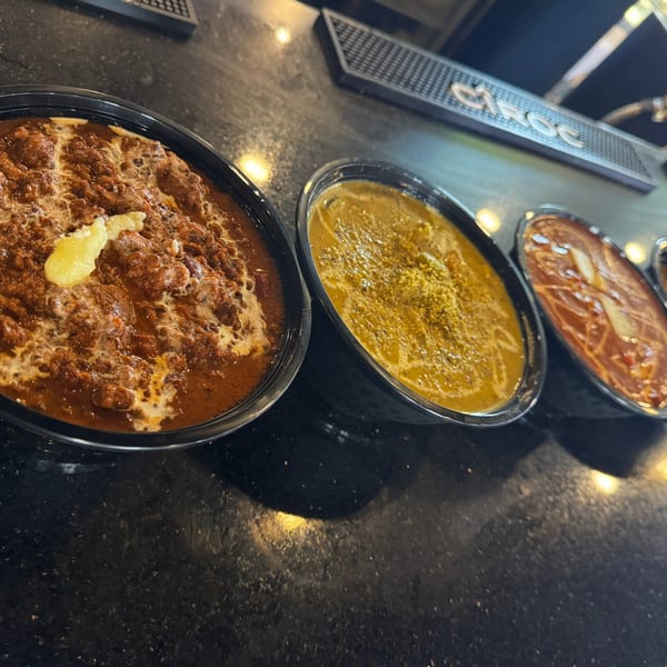 Three bowls of Indian curries, one with a dollop of butter, on a dark countertop.