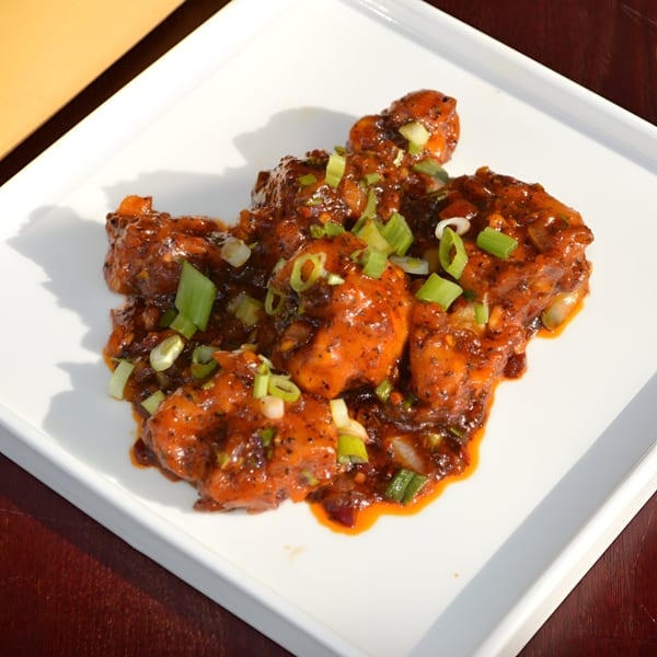 Spicy Indian chicken dish, garnished with chopped green onions, served on a white square plate.