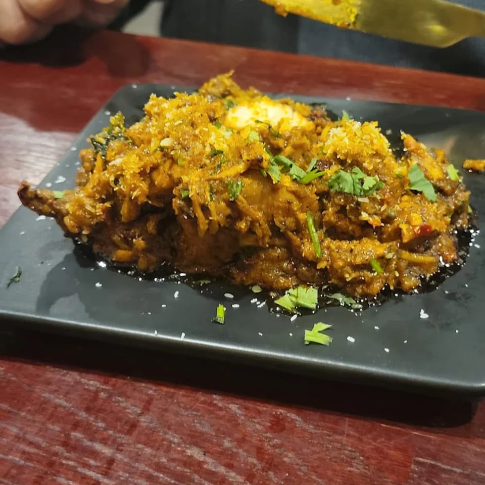 A vibrant Indian dish from Spice Kitchen, garnished with fresh cilantro and white sprinkles, on a black plate.