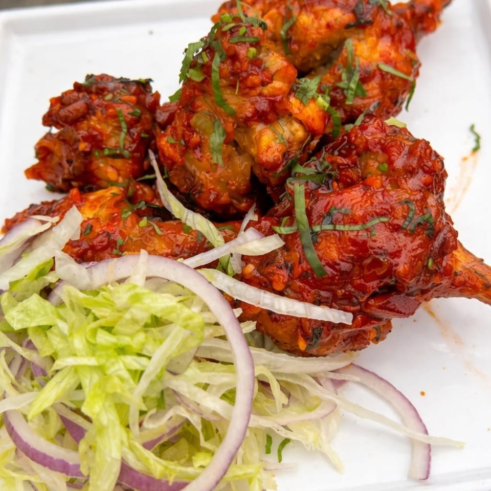 Spicy red chicken lollipops garnished with fresh herbs, shredded lettuce, and red onion.
