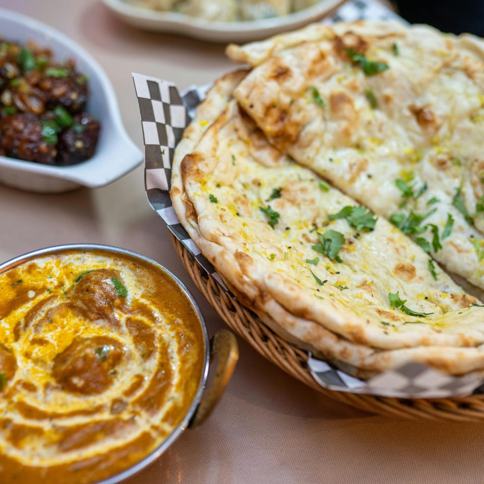 Indian butter chicken, garlic naan in a basket, and chili chicken on a table at Spice Kitchen.