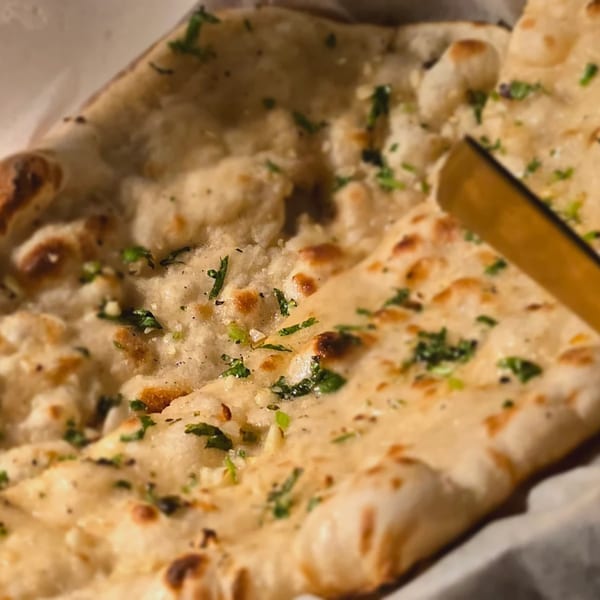 Close-up of golden-brown naan bread, sprinkled with fresh green herbs and spices, from Spice Kitchen.