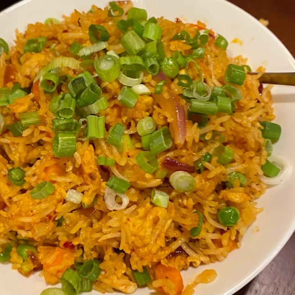 Close-up of Indian fried rice with chicken, vegetables, and green onions in a white bowl.