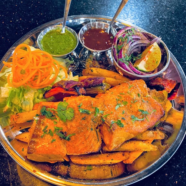 Indian salmon tikka with fries, salad, and sauces on a silver platter at Spice Kitchen.