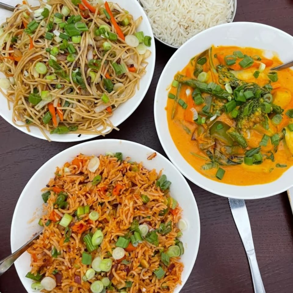 Three bowls of Indian food: noodles, fried rice, and a vegetable curry, all garnished with scallions.